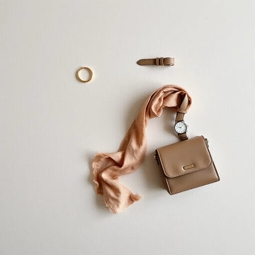 Neatly arranged trendy accessories with jewelry, a watch, a belt, a scarf, and a mini bag on a neutral background